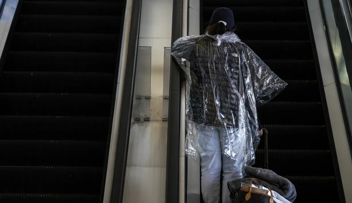 Seorang perempuan dengan jas hujan sekali pakai menaiki eskalator di Bandara Internasional Los Angeles di Los Angeles, California, 23 November 2020. Menjelang Thanksgiving, Pusat Pengendalian Penyakit mengimbau agar orang Amerika tak bepergian di tengah lonjakan Covid-19 di AS. (AP Photo/Jae C. Hong