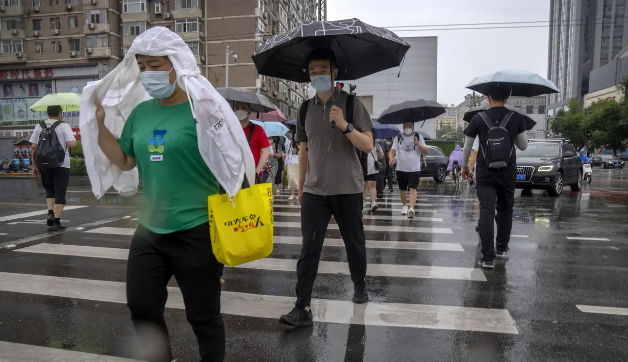 <p>Para komuter berjalan melintasi penyeberangan selama jam sibuk pagi hari pada hari hujan di Beijing, Rabu (29/6/2022). Pemerintah China mengurangi masa karantina wajib untuk pelancong yang merupakan pelonggaran pertama yang diterapkan negara itu kepada turis sejak Covid-19 merebak. (AP Photo/Mark Schiefelbein)</p>