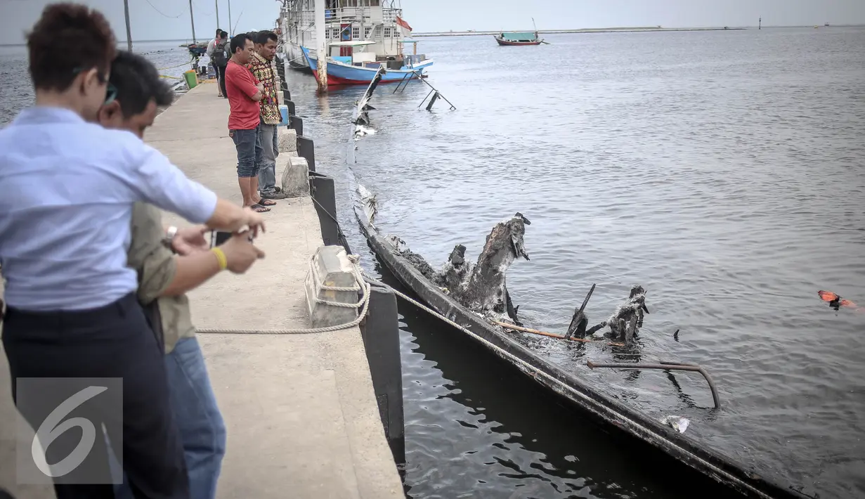 Sejumlah warga melihat bangkai kapal Zahro yang terlihat hangus di pelabuhan Muara Angke, Jakarta, Selasa (3/1). Bangkai Kapal Zahro Express rencananya akan diangkat ke daratan Dermaga Pelabuhan Muara Angke. (Liputan6.com/Faizal Fanani)