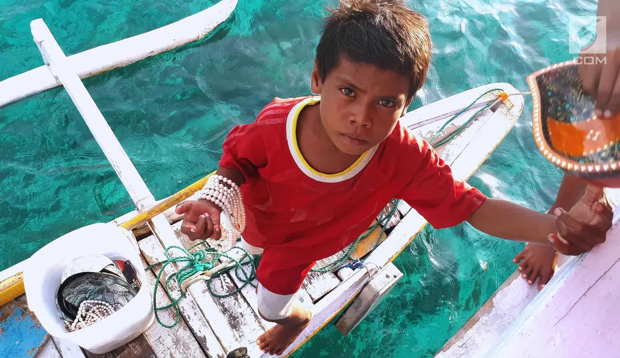 Albin berusaha naik ke atas kapal semi pinisi dengan membawa barang dagangan di Pink Beach, Taman Nasional Komodo, Sabtu, (9/10). Albin bersama saudara kandungnya, Kevin berjualan dari pagi hingga sore hari. (Liputan6.com/Fery Pradolo)