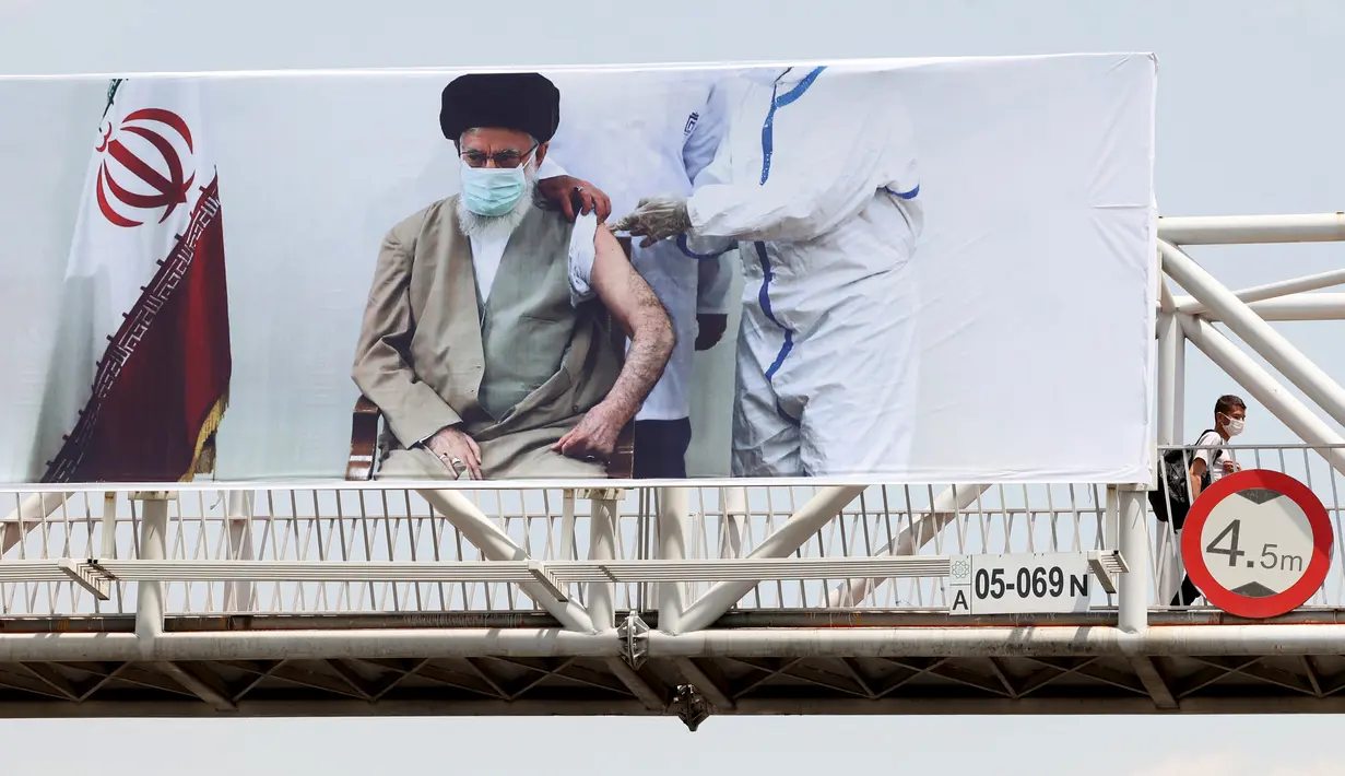 Seorang pria melintasi jembatan di mana spanduk yang menunjukkan pemimpin tertinggi Iran Ayatollah Ali Khamenei menerima vaksin COVID-19, di Teheran, Sabtu (3/7/2021). Presiden Hassan Rouhani mengaku khawatir Iran akan dilanda gelombang kelima akibat mewabahnya varian Delta. (ATTA KENARE/AFP)
