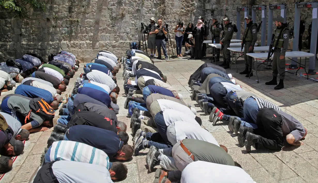 Umat muslim melakukan ibadah di depan komplek Masjid Al-Aqsa dengan penjagaan petugas perbatasan Israel di Yerusalem, Minggu (16/7). Dibukanya kembali komplek tempat suci ini untuk mengurangi kemungkinan kerusuhan yang lebih luas. (AP/Mahmoud Illean)