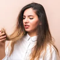 Seorang perempuan berbaju putih sedang memegang rambutnya yang tampak kering dan rusak (Foto Dok: Freepik/user15503477).