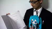 Akihiko Kondo asal Jepang berpose dengan boneka aktris virtual, Hatsune Miku sambil menunjukkan surat nikah mereka di Tokyo, 10 November 2018. Pengalaman traumatis yang 10 tahun lalu membuat pria 35 tahun itu trauma pada wanita. (Behrouz MEHRI/AFP)