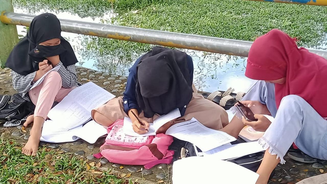 Para pelajar belajar di tepi sungai karena susah sinyal