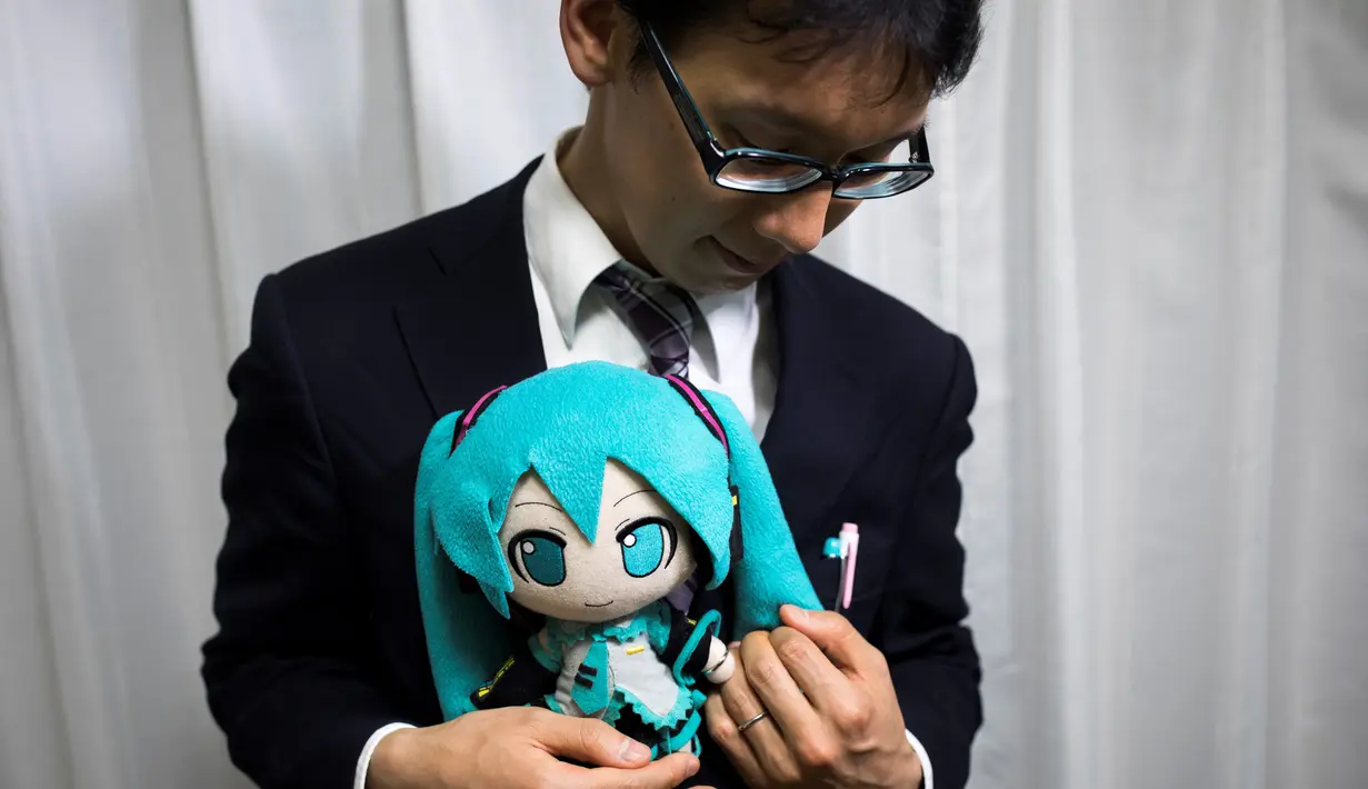 Akihiko Kondo asal Jepang berpose dengan boneka aktris virtual, Hatsune Miku sambil mengenakan cincin kawin mereka di Tokyo, 10 November 2018. Pria berusia 35 tahun itu memutuskan menikah dengan boneka anime pada 4 November lalu. (Behrouz MEHRI/AFP)