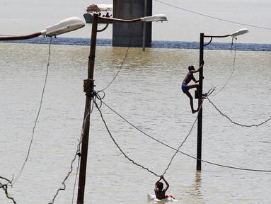 Warga memanjat tiang listrik saat terjebak banjir di tepi sungai Gangga, Allahabad, India, (21/8). Banjir bandang menerjang sejumlah wilayah di India yang menyebabkan banyak warga yang terjebak. (REUTERS/Jitendra Prakash)