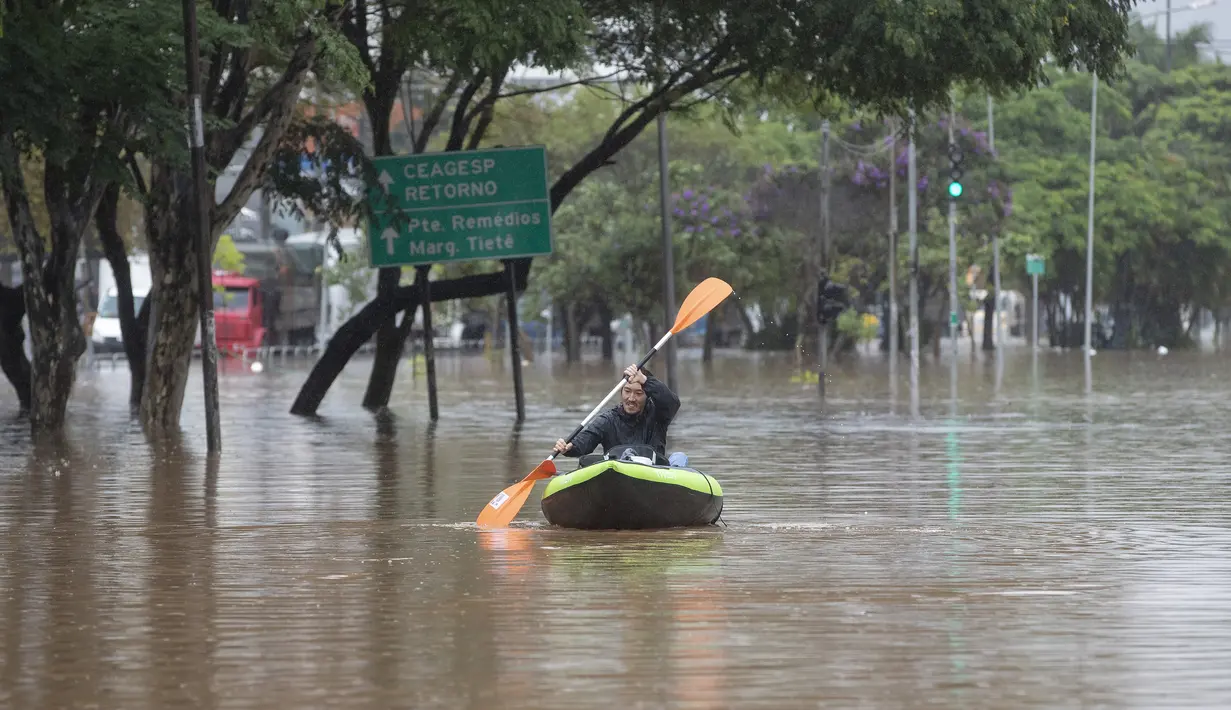 Seorang pria mendayung kayak di sepanjang jalan yang banjir di Sao Paulo, Brasil, Senin, (10/2/2020). Hujan deras yang membanjiri kota, menyebabkan pinggir sungai utama meluap. (AP Photo/Andre Penner)