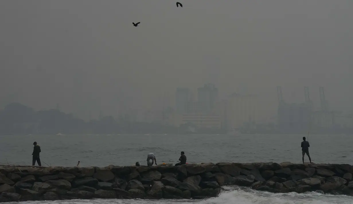 Orang-orang memancing saat asap dan kabut menyelimuti cakrawala di Kolombo, Sri Lanka, Jumat, 9 Desember 2022. Udara tercemar dari negara tetangga India memperparah masalah polusi. (AP Photo/Eranga Jayawardena)