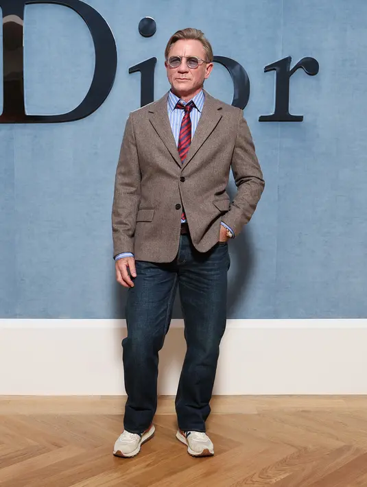 Daniel Craig terlihat awet muda dengan kombinasi stripe shirt and tie. Dilapisi dengan casual blazer, denim pants, dan sneakers [Dior]