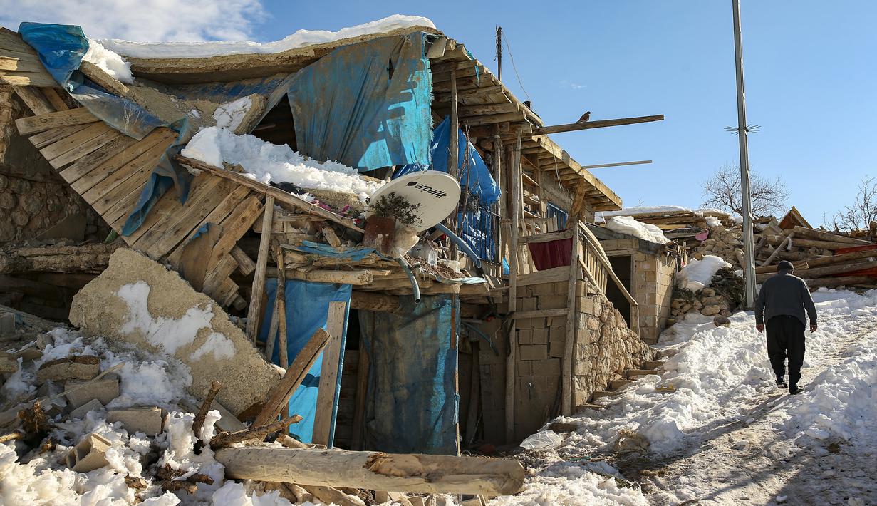 Seseorang berjalan melewati rumah-rumah yang runtuh di desa Buyuknacar di Kahramanmaras, Turki, Rabu, 15 Februari 2023. Sementara jumlah korban tewas hampir pasti akan meningkat lebih jauh lagi, banyak dari puluhan ribu korban selamat yang kehilangan tempat tinggal masih berjuang untuk memenuhi kebutuhan dasar, seperti mencari perlindungan dari hawa dingin yang menggigit. (AP Photo/Emrah Gurel)
