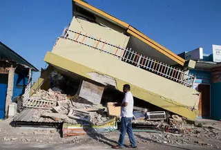 Seorang pria berjalan melewati bangunan yang runtuh akibat gempa di Reo, provinsi Nusa Tenggara Timur, Indonesia, Senin, 17 Agustus 2026. (AP Photo/Firdia Lisnawati)