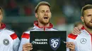 Bek Jerman,  Benedikt Hoewedes memegang tulisan ucapan turut berbelasungkawa kepada para korban jatuhnya pesawat Germanwings di Pegunungan Alpen di Stadion Fritz-Walter, Kamis (26/3/2015). Jerman bermain Imbang 2-2 atas Australia. (REUTERS/Ralph Orlowski)
