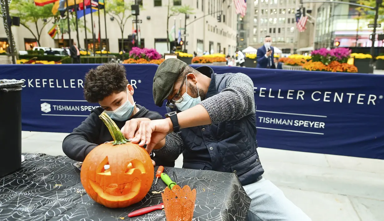 Sharif Butler dan keponakannya Chace mengukir labu di Rockefeller Center (22/10/2020). Para pekerja di Rockefeller Center beristirahat sejenak untuk mempelajari cara mengukir labu dengan benar dari Maniac Pumpkin Carvers, seniman dari Brooklyn . (Diane Bondareff/AP Images for Tishman Speyer)