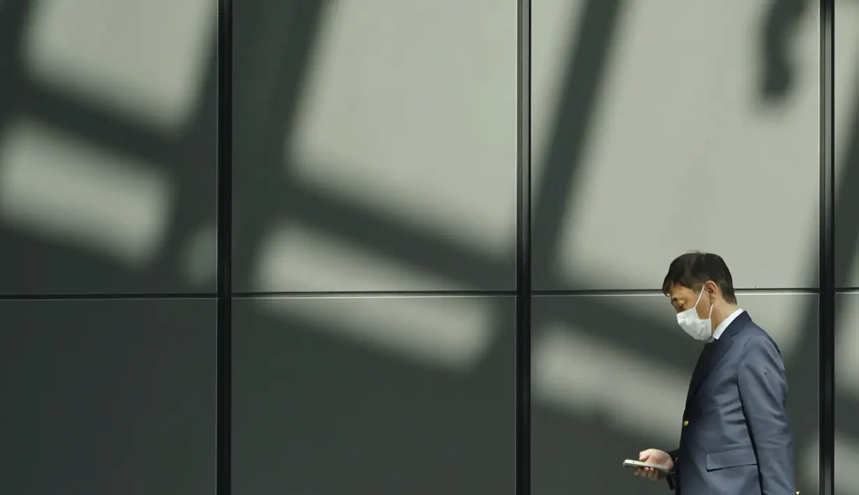 Seorang pria yang mengenakan masker pelindung untuk membantu mencegah penyebaran virus corona berjalan di sebuah gedung di Tokyo, Selasa (6/4/2021). Ibukota Jepang mengonfirmasi lebih dari 390 kasus virus korona baru pada hari Selasa. (AP Photo/Eugene Hoshiko)
