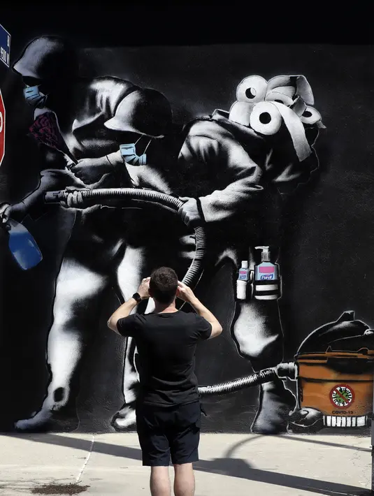 Seorang pria memotret mural bertema virus corona COVID-19 di Los Angeles, Amerika Serikat, Selasa (14/4/2020). (AP Photo/Marcio Jose Sanchez)