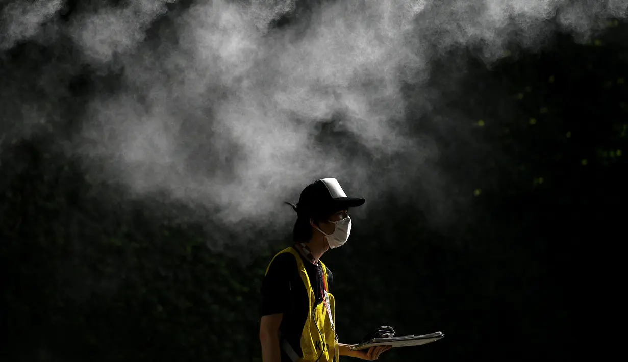 Seorang relawan berjalan di bawah alat penyemprot desinfektan di Tokyo pada 21 Juli 2021 menjelang Olimpiade Tokyo 2020. (AFP/Mohd Rasfan)