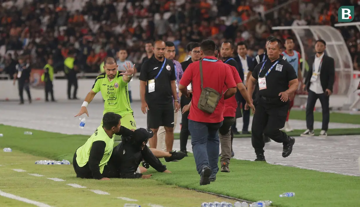 Kiper Persija Jakarta, Andritany Ardhiyasa (kiri) berusaha menyelamatkan pendukung yang masuk ke lapangan setelah laga melawan Persita Tangerang dalam pertandingan pekan ke-21 BRI Liga 1 2023/2024 yang berlangsung di Stadion Utama Gelora Bung Karno, Jakarta, Minggu (3/12/2023) malam WIB. (Bola.com/M Iqbal Ichsan)