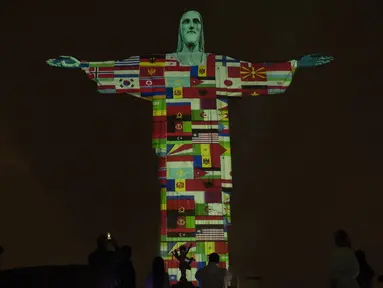 Patung Christ the Redeemer bermandi cahaya bendera negara-negara yang saat ini terpapar virus corona COVID-19 di Rio de Janeiro, Brasil, Rabu (18/3/2020). Pertunjukan ini untuk menunjukkan dukungan bagi mereka yang menderita virus corona COVID-19. (AP Photo/Silvia Izquierdo)