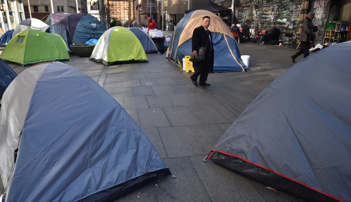Pejalan kaki melewati deretan tenda yang didirikan para tunawisma di kawasan Martin Place, pusat kota Sydney, 2 Agustus 2017. Di perkampungan tenda para tunawisma itu mereka bertahan hidup dengan membuka lapak di pinggir jalan. (PETER PARKS / AFP)