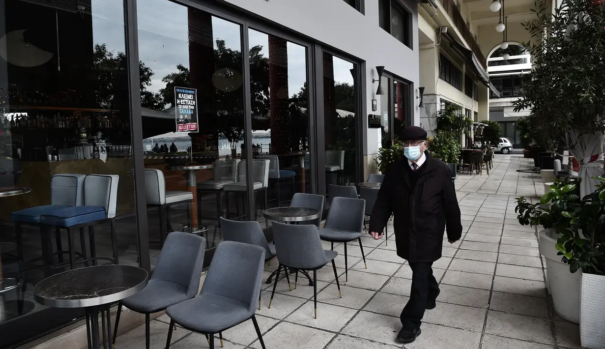 Seorang pria berjalan melewati kafe dan restoran yang tutup di Thessaloniki, Yunani, Selasa (16/11/2021). Pemilik restoran, kafe, dan bar melakukan pemogokan selama 24 jam, memprotes aturan terkait Covid-19 dan biaya energi yang tinggi. (Sakis MITROLIDIS / AFP)