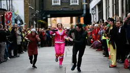 Para peserta berlari membawa wajan berisi pancake dalam acara tahunan Great Spitalfields Pancake Race di London, Inggris, Selasa (9/2). Dalam lomba itu, peserta diwajibkan berlari sambil membalik pancake tanpa membuatnya terjatuh. (REUTERS/Stefan Wermuth)