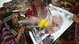 Dukun Peru menyemprotkan air ke foto Presiden Meksiko Andres Manuel Lopez Obrador saat memberikan prediksi untuk 2022 dalam ritual tradisional sebelum Malam Tahun Baru di bukit San Cristobal di Lima, Peru  (29/12/2021). (AFP/Ernesto Benavides)