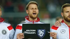 Bek Jerman,  Benedikt Hoewedes memegang tulisan ucapan turut berbelasungkawa kepada para korban jatuhnya pesawat Germanwings di Pegunungan Alpen di Stadion Fritz-Walter, Kamis (26/3/2015). Jerman bermain Imbang 2-2 atas Australia. (REUTERS/Ralph Orlowski)