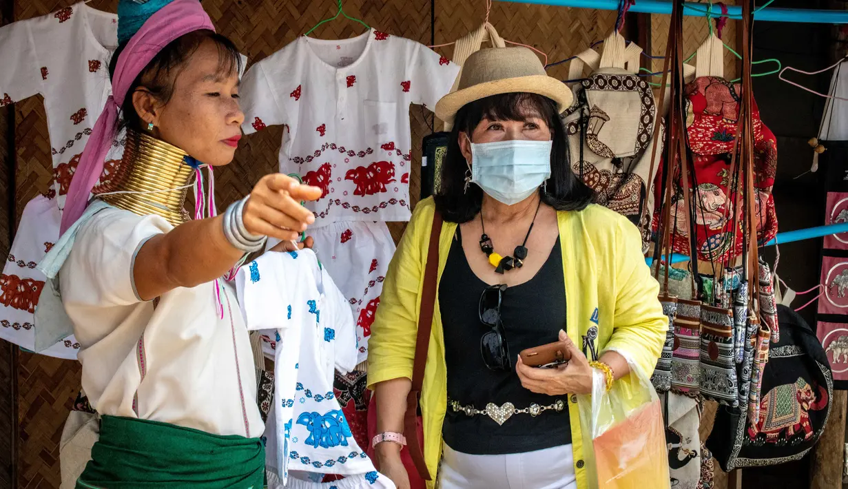 Perempuan Suku Kayan berbicara dengan turis yang mengenakan masker di sebuah toko suvenir di Taman Chang Siam, Pattaya, Thailand, Rabu (12/2/2020). Chang Siam Park adalah salah satu primadona bagi wisatawan China di Pattaya  yang kini berangsur sepi karena virus corona. (Mladen ANTONOV / AFP)