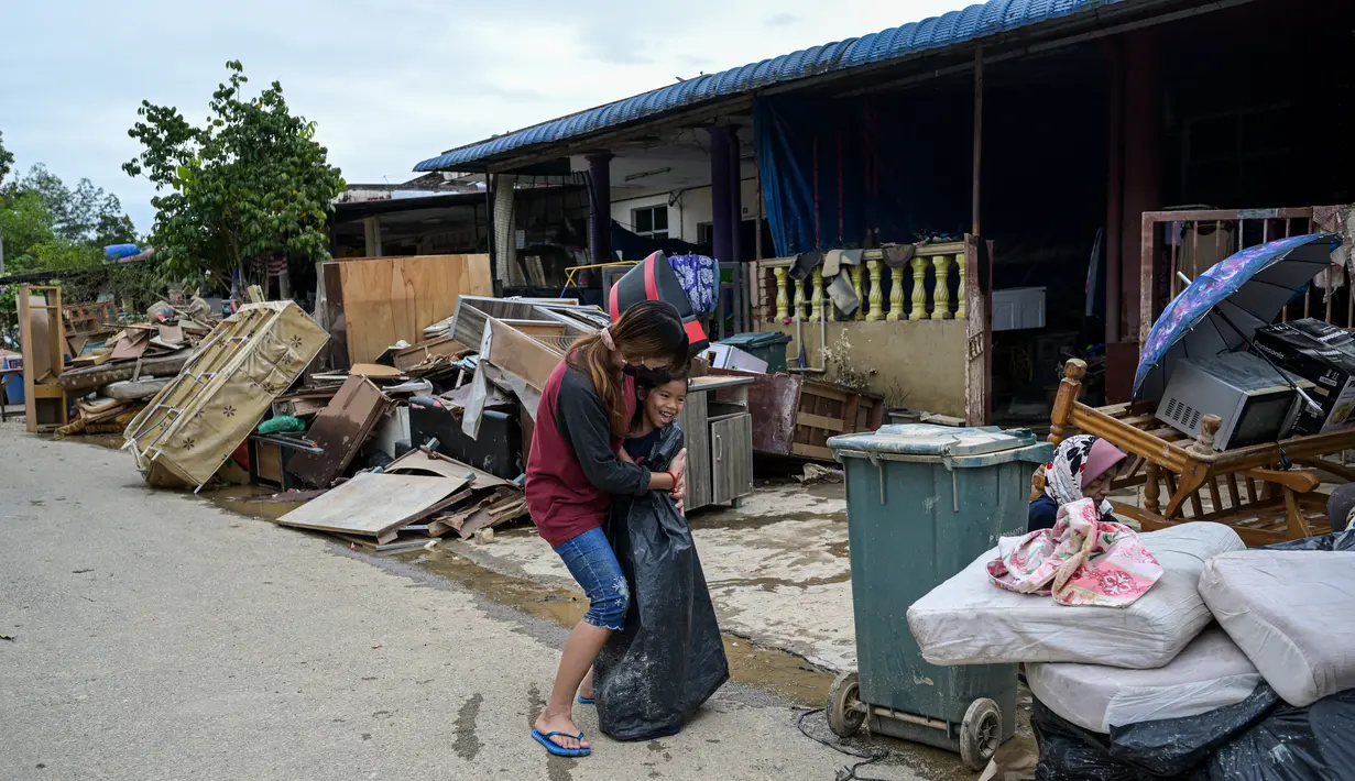 Seorang wanita memeluk anak di dekat puing-puing dan barang-barang di luar rumah mereka, setelah banjir surut di Mentakab, negara bagian Pahang Malaysia (11/1/2021). Banjir yang melanda daerah tersebut, membuat  Puluhan ribu warga dievakuasi. (AFP/Mohd Rasfan)