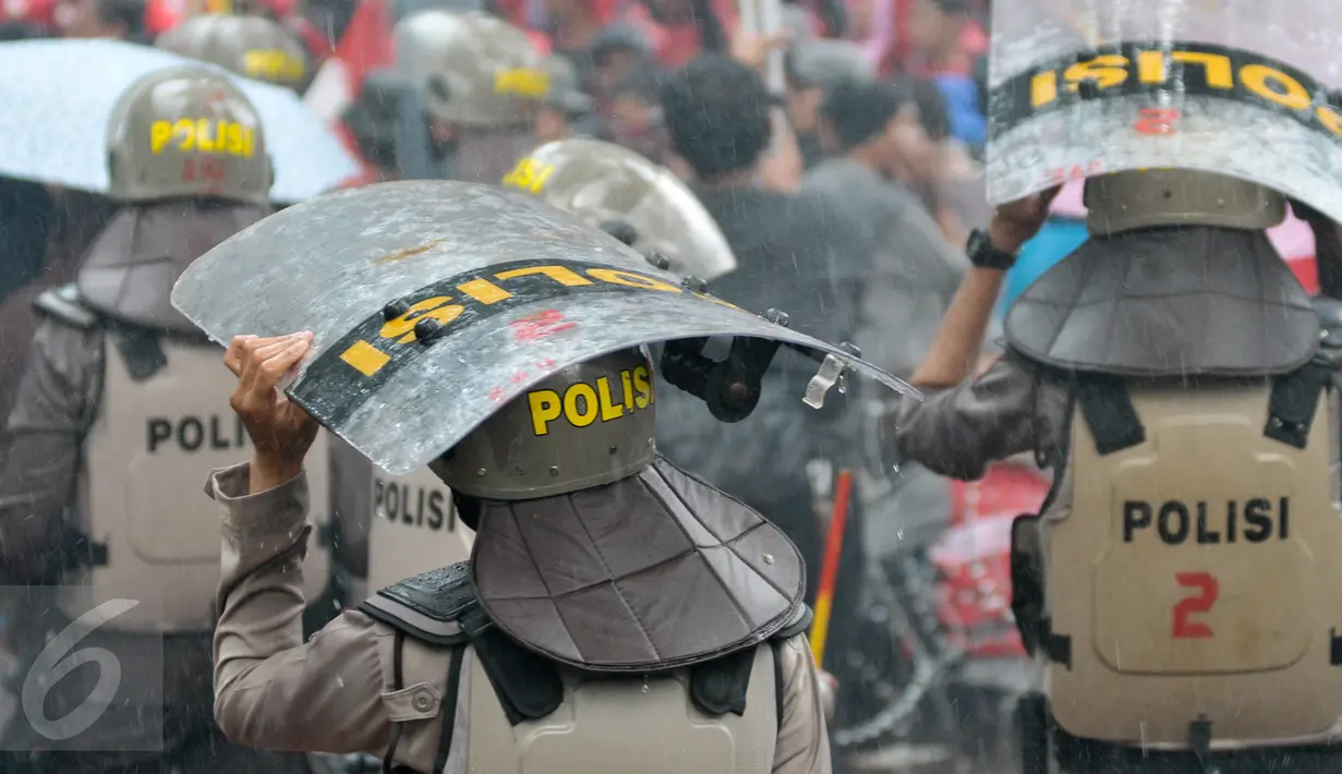 Petugas kepolisian menggunakan tameng untuk berteduh dari hujan saat menjaga aksi Hari Buruh di Jalan Medan Merdeka, Jakarta, Senin (1/5). (Liputan6.com/ Yoppy Renato)