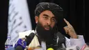 Di depan bendera Taliban, juru bicara Taliban Zabihullah Mujahid berbicara pada konferensi pers pertamanya, di Kabul, Afghanistan, pada Selasa (17/8/2021). Mujahid yang selama ini misterius, muncul pertama kalinya di hadapan wartawan pada Selasa waktu setempat. (AP Photo/Rahmat Gul)