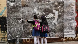 Dua anak sekolah melihat foto jurnalistik karya Sara Blesener, Kolombia (1/11). Karya ini diprakarsai oleh Dysturb, sebuah komunitas jurnalis foto yang berkeinginan membuat informasi visual secara bebas diakses oleh khalayak luas. (AFP PHOTO/luis acosta)