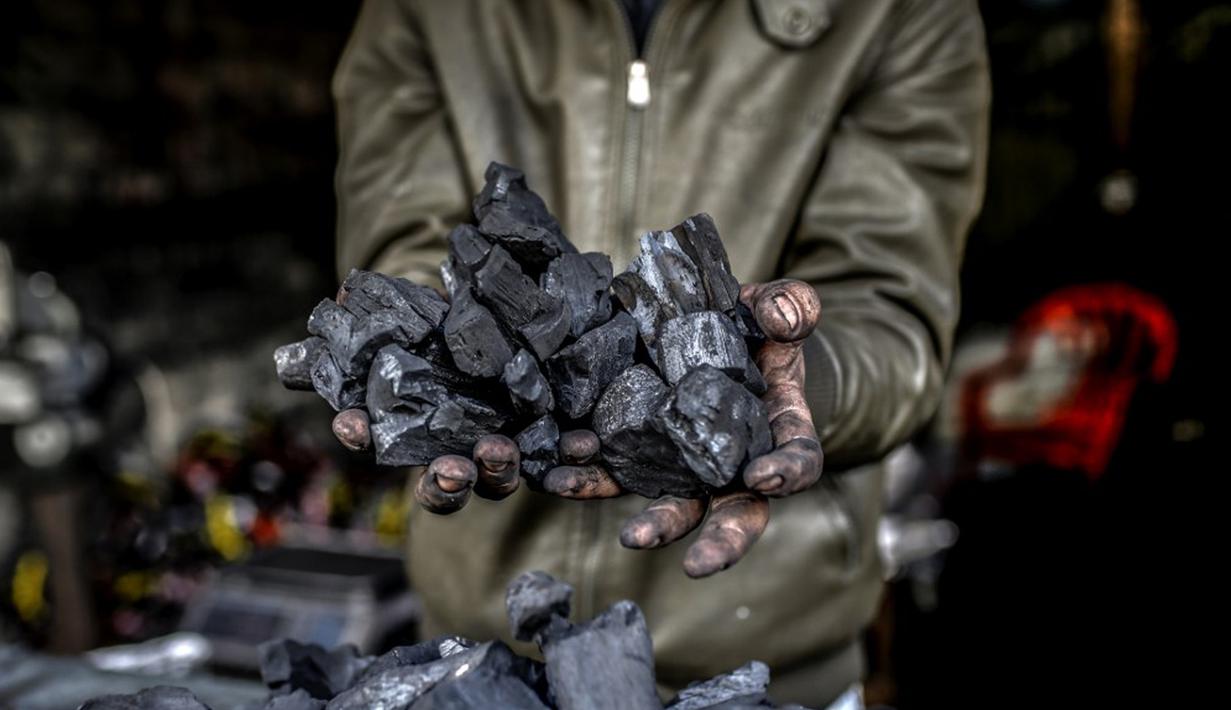 Seorang pekerja menunjukkan segenggam arang di fasilitas produksi arang al-Hattab, sebelah timur Kota Gaza, Palestina, 28 Januari 2021. Satu kilogram arang dijual seharga USD 1,50 di tempat dan USD 2,50 di pasar. (Mohammed ABED/AFP)