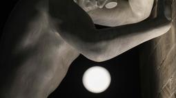 Bulan purnama muncul di atas patung 'Mr Arbitrium' karya seniman Italia Emanuele Giannelli bersandar ke Peace Arch, di Milan, Italia, Rabu (13/7/2022). Bulan Purnama dikenal sebagai Buck Moon dan juga Supermoon. Fenomena tersebut hanya terjadi setiap 9 tahun sekali, dan terakhir kali muncul pada 2013 lalu. (AP Photo/Luca Bruno)