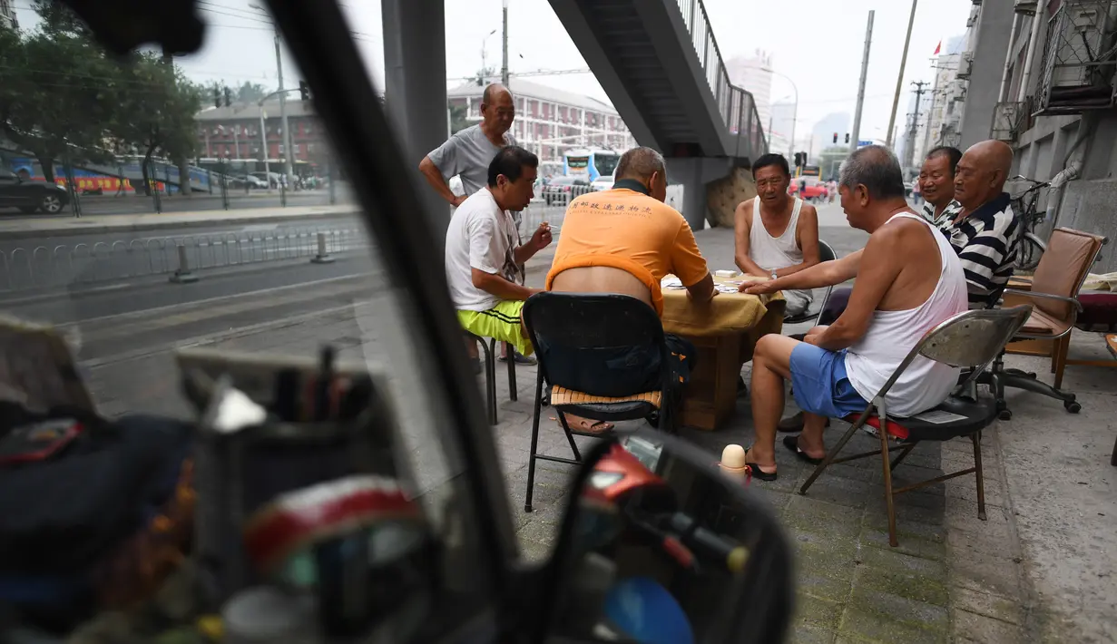 Suasana sekelompok pria bermain kartu remi di trotoar di luar gedung apartemen di Beijing, China (10/8). Di Indonesia sendiri akrab dengan istilah permainan “41”, truf, “remi”, “cangkulan”, dsb. (AFP Photo/Greg Baker)