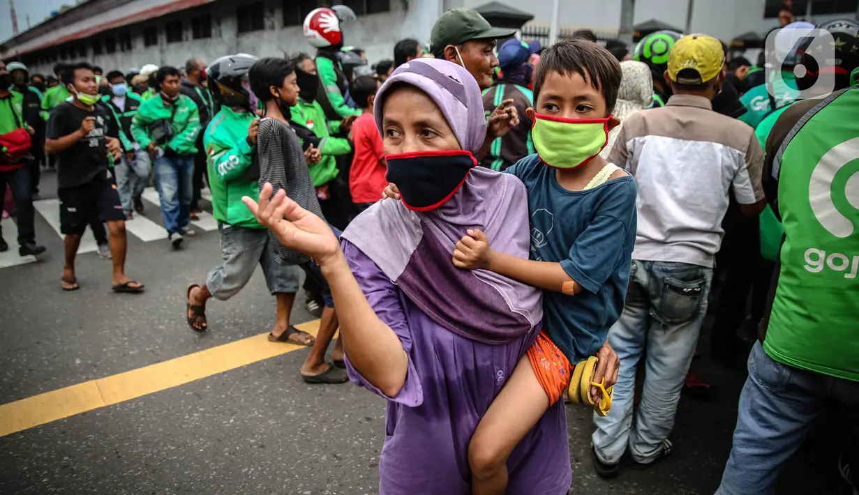 Seorang wanita menggendong anak  kecil saat mengantre nasi kotak serta masker dari TNI di Markas Komando Gabungan Wilayah I, Jakarta, Selasa (21/4/2020). Dalam rangka Hari Kartini, TNI membagikan makanan dan masker kepada masyarakat. (Liputan6.com/Faizal Fanani)