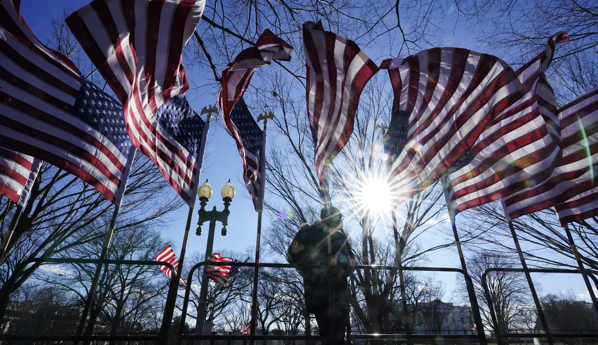 Seorang pekerja memasang bendera di depan While House sebagai persiapan upacara pelantikan Presiden terpilih Joe Biden di Washington, Selasa (19/1/2021). Pelantikan Joe Biden berlangsung di tengah ancaman kekerasan dari massa pendukung Donald Trump dan pandemi Covid-19. (AP Photo/David Goldman)
