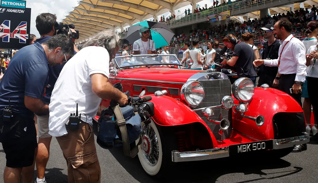 Pembalap Formula 1 Mercedes asal Inggris, Lewis Hamilton menggunakan payung berada di mobil Mercedes-Benz klasik saat mengikuti parade jelang Grand Prix Formula 1 Malaysia di Sirkuit Internasional Sepang, Malaysia, (2/10). (REUTERS/Edgar Su)
