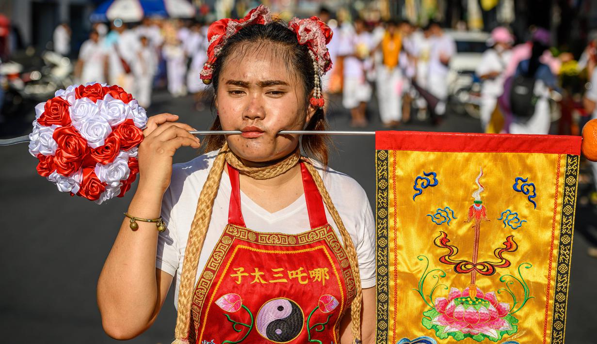 Seorang wanita menusuk pipinya dengan besi  saat mengikuti prosesi perayaan Festival Vegetarian tahunan di Phuket, Thailand, Kamis (3/10/2019). Festival ini biasanya berlangsung selama 9 hari di akhir September sampai Oktober. (AFP Photo/Mladen Antonov)