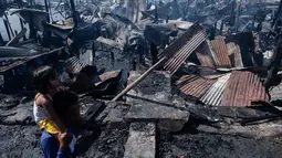 Seorang pria menggendong anaknya setelah rumah-rumah mereka hangus terbakar di sebuah daerah kumuh di Navotas, Manila (8/11). Dilaporkan sekitar 150 keluarga terkena dampak kebakaran tersebut. (AFP Photo/Noel Celis)