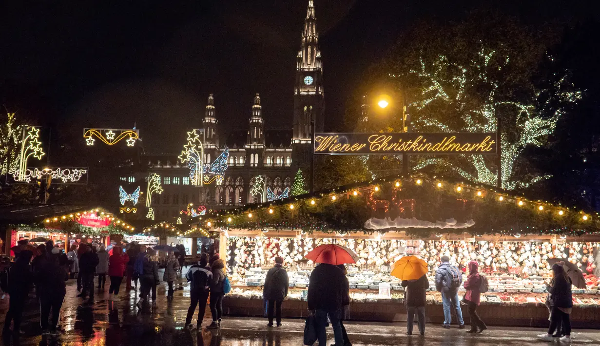 Wisawatan menerobos hujan saat mengunjungi pasar Natal di luar City Hall, Wina pada 26 November 2018. Christkindlmarkt menjadi ciri khas Natal dan musim dingin di Austria dan juga Jerman yang sudah sejak pertengahan tahun 1310. (JOE KLAMAR / AFP)