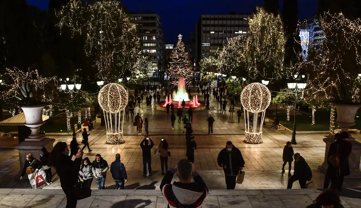 Orang-orang mengambil gambar alun-alun Syntagma yang diterangi dekorasi Natal di pusat kota Athena, Yunani pada 21 Desember 2020. Yunani akan merayakan musim Natal di bawah langkah-langkah penguncian wilayah atau lockdown COVID-19 hingga 7 Januari 2021 mendatang. (LOUISA GOULIAMAKI/AFP)