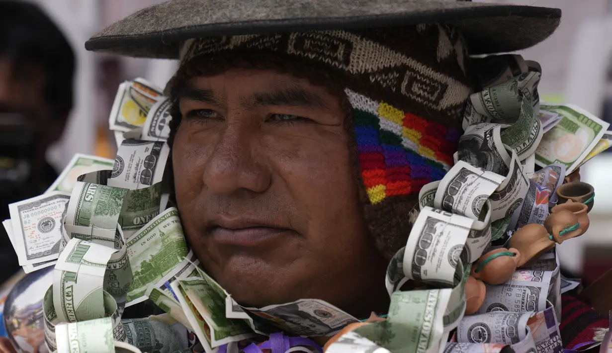 Seseorang berpakaian seperti Ekeko, Dewa Kemakmuran, diselimuti uang palsu pada hari pembukaan Pameran Alasita tahunan, di mana Ekeko adalah tokoh utamanya di El Alto, Bolivia, Selasa (24/1/2023). Orang-orang membeli replika kecil dari hal-hal yang ingin mereka peroleh sepanjang tahun, seperti rumah, mobil, dan kekayaan. Kata Aymara "Alasita" berarti "belikan aku". (AP Photo/Juan Karita)