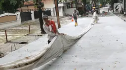 Pekerja menutupi beton yang sudah di cor dengan kain di Jalan Pejaten Raya di Jakarta Selatan (22/11). Proyek pembetonan dan peninggian badan jalan ini guna mengantisipasi banjir yang kerap terjadi di kawasan tersebut. (Liputan6.com/Immanuel Antonius)