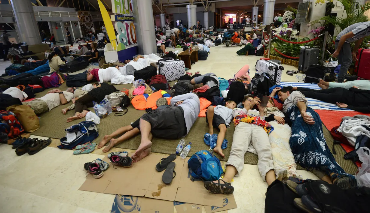 Turis asing bersantai dengan alas seadanya di lantai Bandara Internasional Lombok Praya, NTB, Senin (6/8). Imbas gempa 7 skala Richter, para wisatawan mancanegara terlantar di bandara karena jam pemberangkatan pesawat yang tertunda. (AFP/SONNY TUMBELAKA)