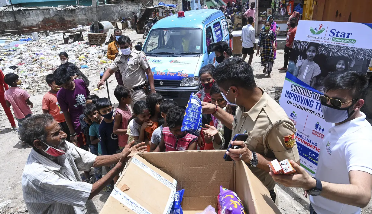 Seorang polisi dan relawan memberikan makanan ringan kepada anak-anak setelah memberikan sampel swab untuk pengujian virus corona Covid-19 di dalam sebuah van di New Delhi, India (1/7/2021).  (AFP/Prakash Singh)