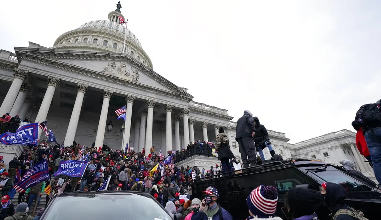 Massa pendukung Presiden Amerika Serikat Donald Trump berdiri di atas kendaraan polisi di Capitol Hill, Washington, Amerika Serikat, Rabu (6/1/2021). Kericuhan terjadi saat massa pendukung Donald Trump merangsek masuk ke dalam Gedung Capitol Hill. (AP Photo/Julio Cortez)
