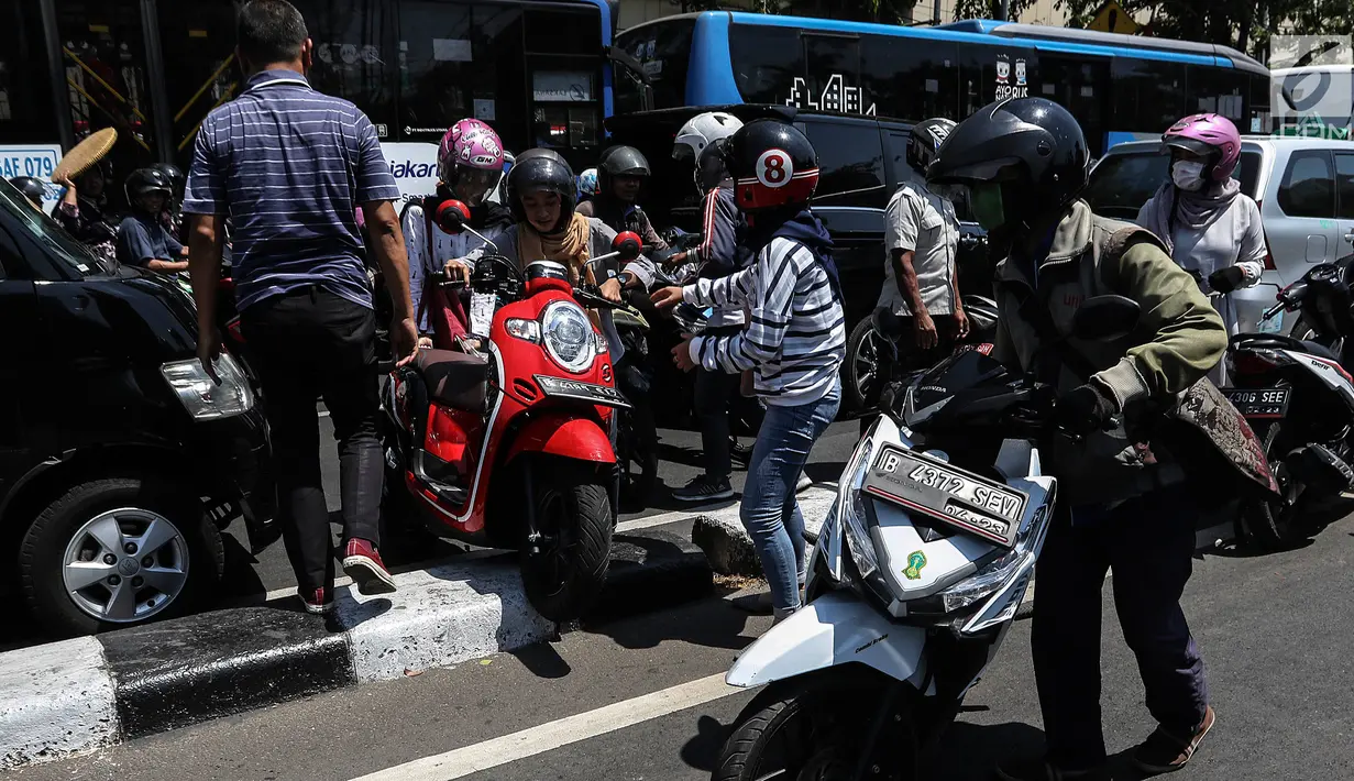 Pengendara berusaha pindah jalur dengan mengangkat sepeda motor mereka melewati pembatas jalan di kawasan Ridwan Rais, Jakarta, Rabu (21/8/2019). Pengendara motor tersebut berpindah jalur disebabkan tidak sabar menunggu kemacetan. (Liputan6.com/Johan Tallo)