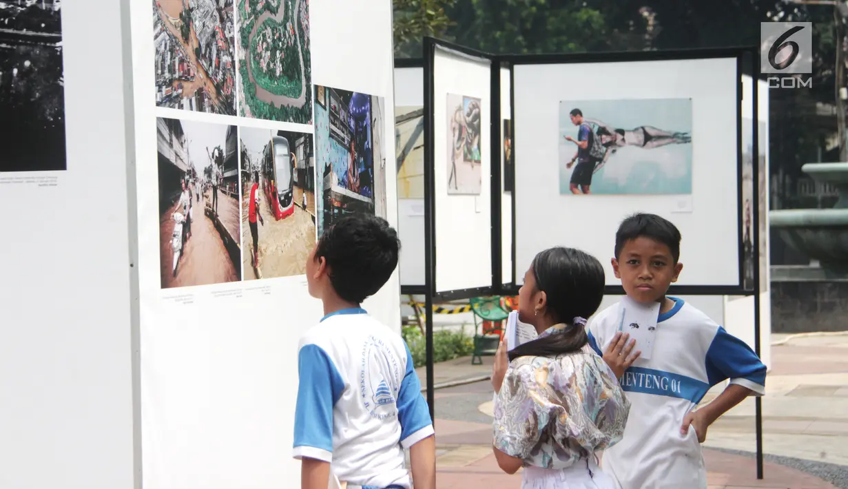 Siswa SD Negeri Menteng 01 mengamati karya foto yang dipamerkan dalam pameran fotografi Rekam Jakarta di Taman Menteng, Kamis (29/8/2019). Kegiatan tersebut dalam rangka edukasi bagi siswa mengenal profesi foto jurnalistik. (Liputan6.com/Marsha Aulia)